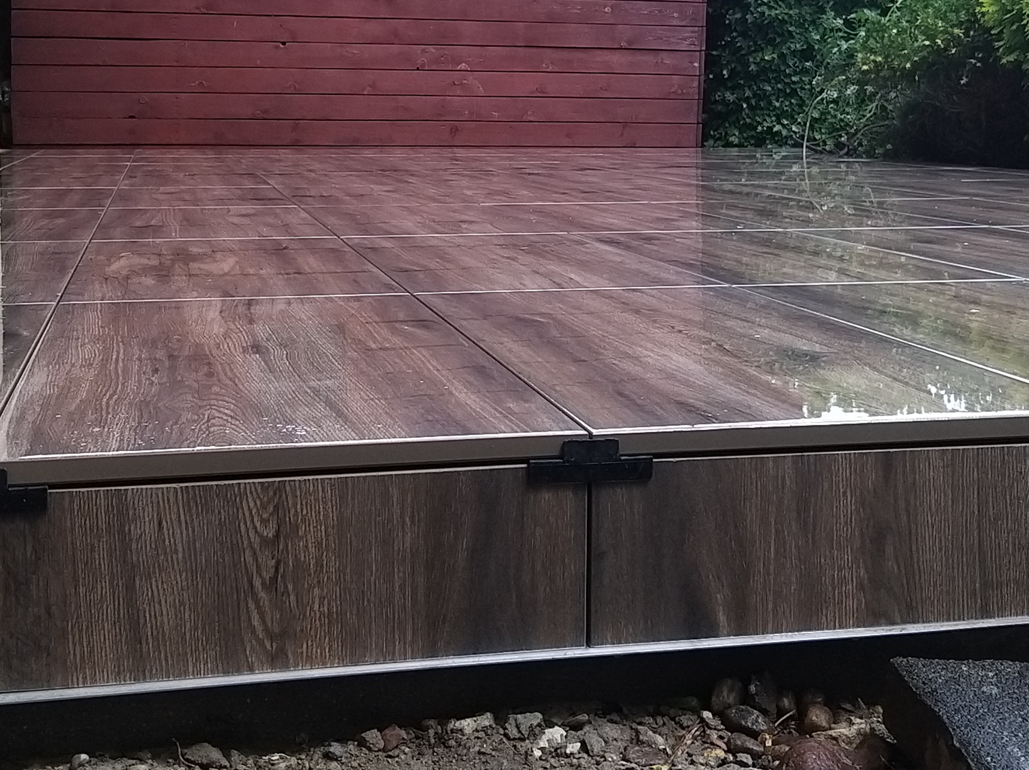 Wykończony taras z brązowych płytek imitujących drewno, z widoczną krawędzią i fragmentem elewacji budynku w tle. Płytki ułożone równo, z fugami. Całość sprawia wrażenie solidnego wykonania.