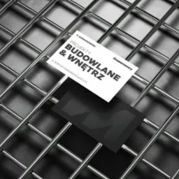 Wizytówki firmy P. Domanowski Projekty Budowlane & Wnętrz na tle metalowej siatki w odcieniach szarości.