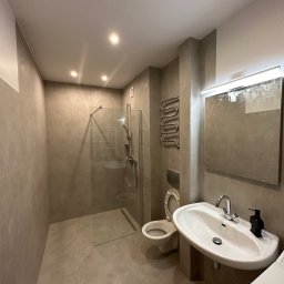 Easybud Vasyl Revych - Wykończona łazienka w odcieniach szarości z kabiną prysznicową typu walk-in, umywalką nablatową, toaletą podwieszaną i grzejnikiem drabinkowym.