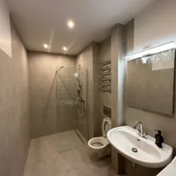 Wykończona łazienka w odcieniach szarości z kabiną prysznicową typu walk-in, umywalką nablatową, toaletą podwieszaną i grzejnikiem drabinkowym.