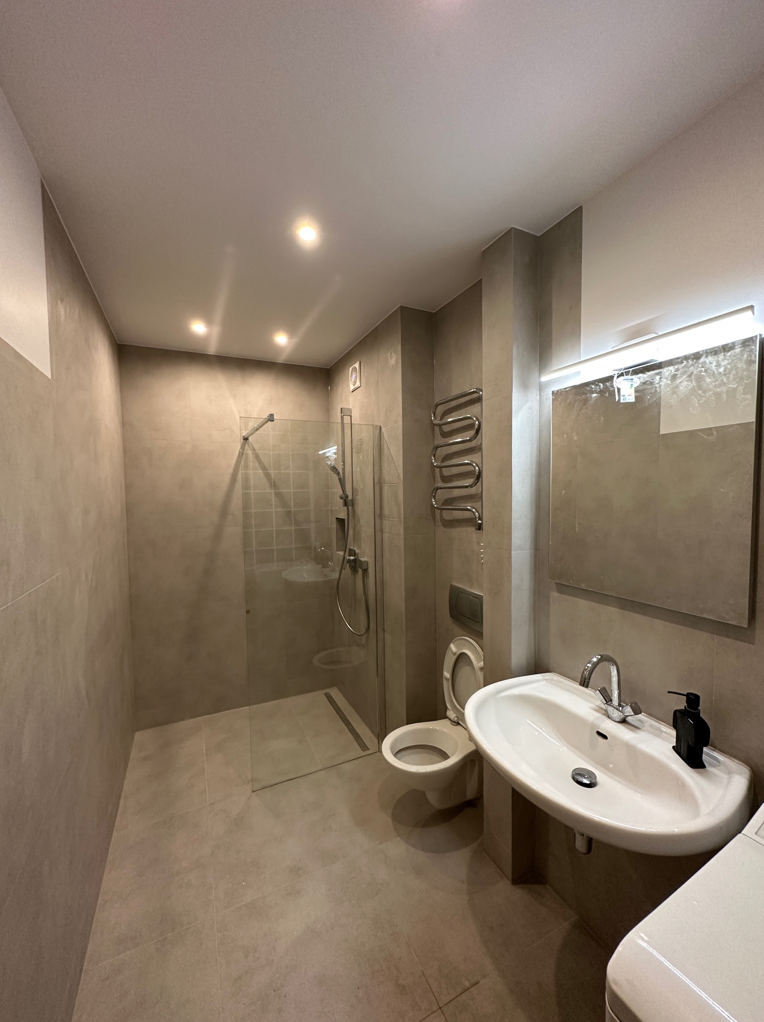 Wykończona łazienka w odcieniach szarości z kabiną prysznicową typu walk-in, umywalką nablatową, toaletą podwieszaną i grzejnikiem drabinkowym.