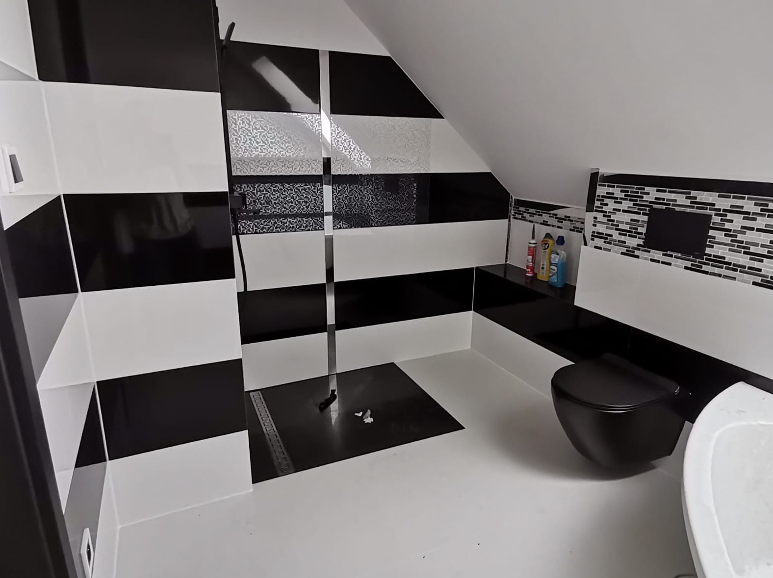 Nowoczesna łazienka na poddaszu z czarno-białymi pasami na ścianach, czarną armaturą i odpływem liniowym w kabinie prysznicowej typu walk-in.