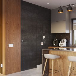 Zulo Design - Nowoczesna kuchnia z drewnianą wyspą, białymi hokerami i czarną ścianą z tablicą kredową, oświetlona trzema lampami wiszącymi. Dekoracyjny zegar na drewnianej ścianie.