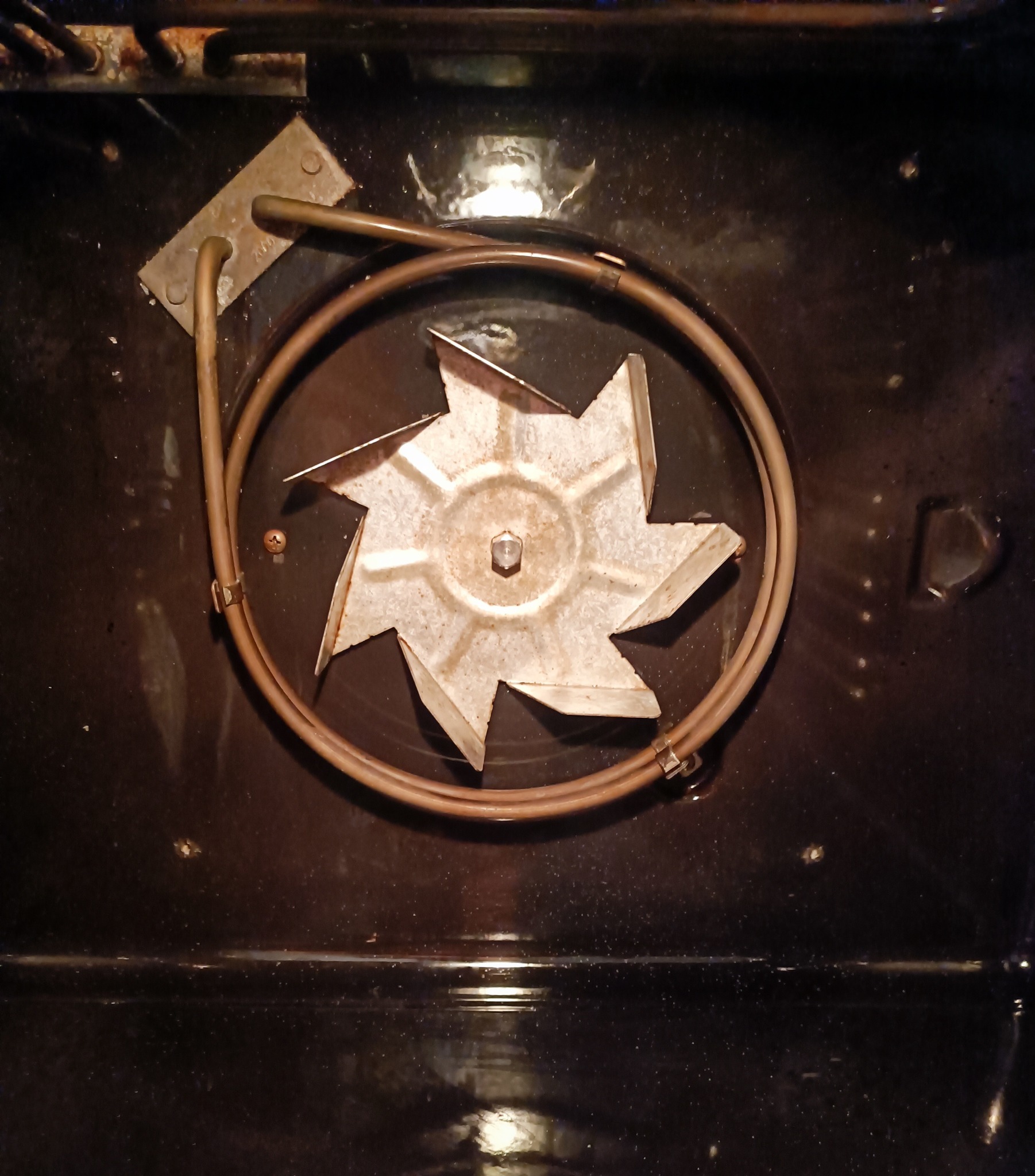 Wnętrze brudnego piekarnika z widoczną grzałką i wentylatorem konwekcyjnym, wymagające dokładnego czyszczenia.