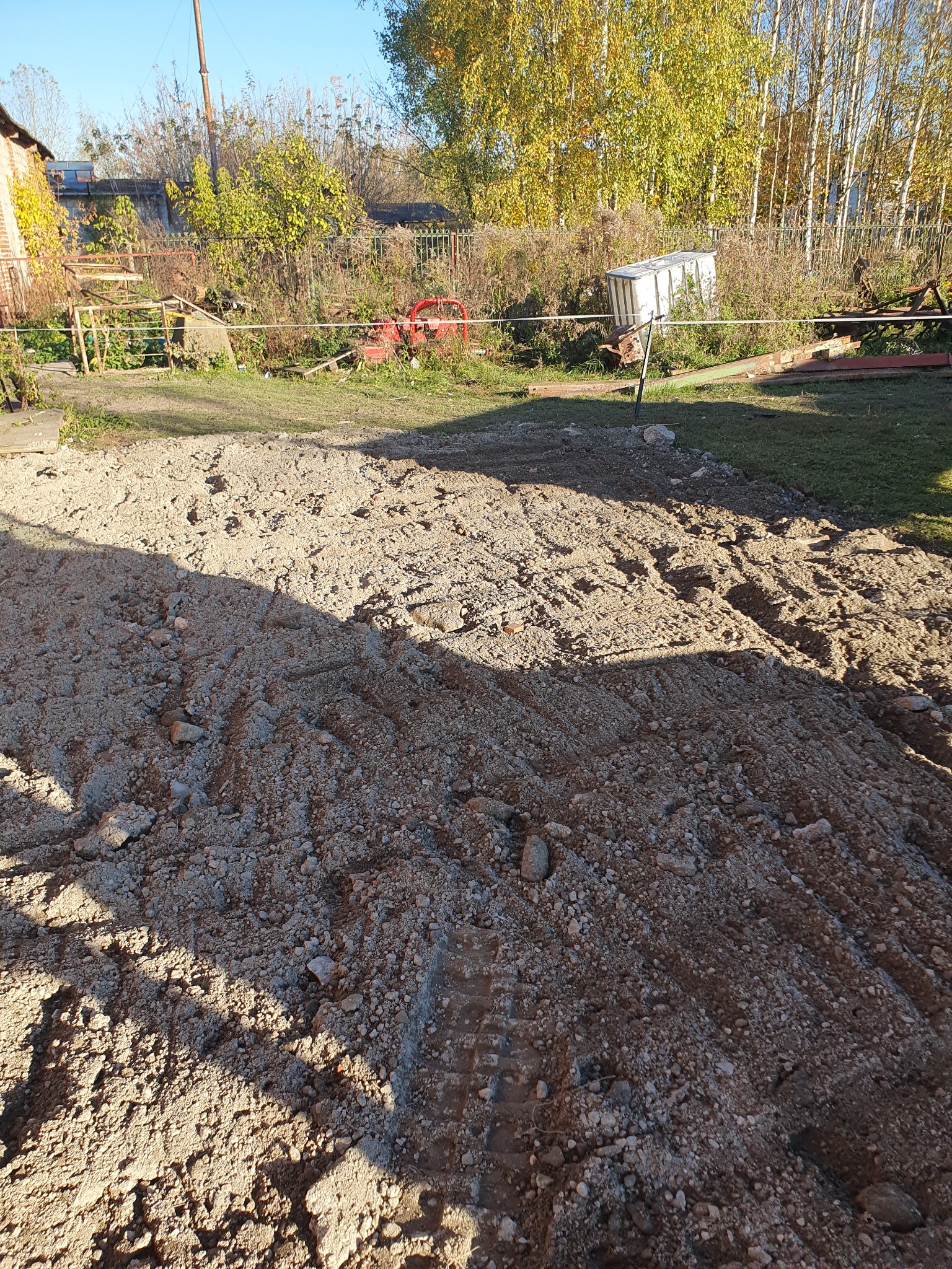 Przygotowany teren pod budowę w Radomiu, widoczne ślady opon na ziemi, w tle zabudowania gospodarcze i drzewa.