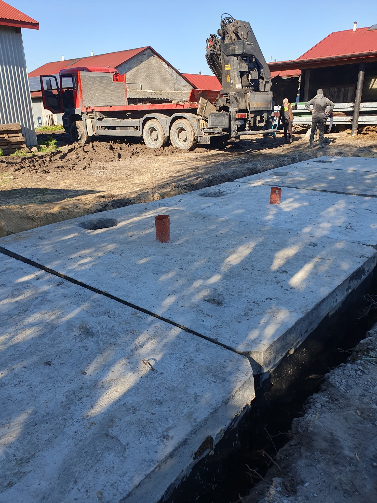 Montaż betonowych płyt fundamentowych z użyciem dźwigu samochodowego na błotnistym terenie budowy.