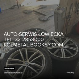 AUTO-SERWIS Tarnowskie Góry KOLMETAL.BOOKSY.COM - Wnętrze warsztatu samochodowego z podnośnikiem i stosem opon z felgami, na jednej z nich widoczne logo BMW.
