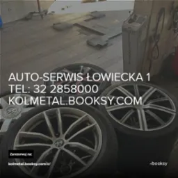 Wnętrze warsztatu samochodowego z podnośnikiem i stosem opon z felgami, na jednej z nich widoczne logo BMW.