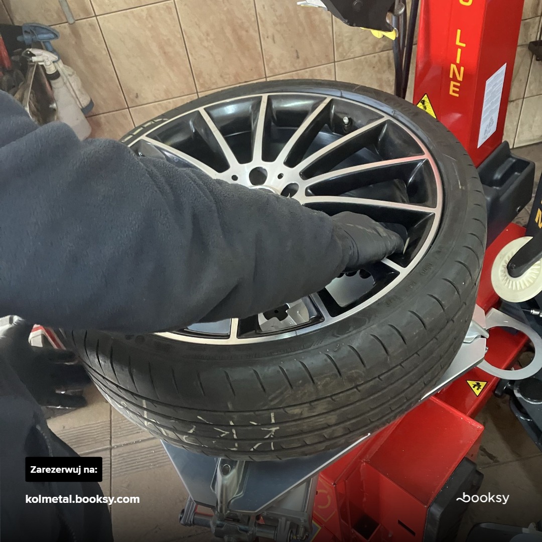 Czarna opona z felgą na czerwonym urządzeniu do wymiany opon, pracownik w czarnych rękawicach wkłada coś do środka felgi.