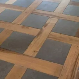 Dekoracyjna podłoga z płytek w odcieniach szarości, ułożonych w kwadraty, obramowanych jasnym drewnem w geometryczny wzór kraty.