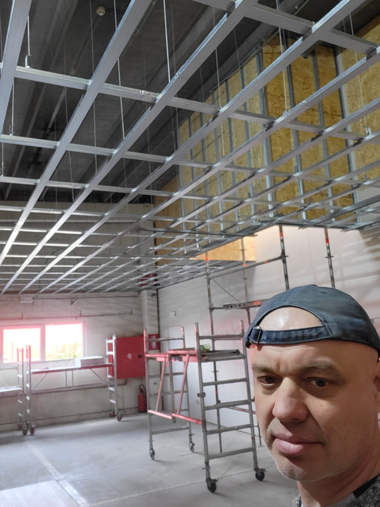 Montaż metalowej konstrukcji podwieszanego sufitu, widok z dołu, pracownik w kadrze.