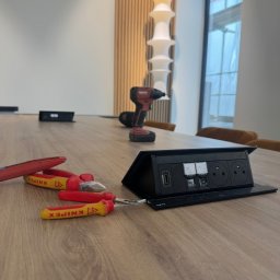 VoltSky Szymon Zaremba - Wpuszczana listwa zasilająca z gniazdami elektrycznymi, HDMI i USB na drewnianym stole, obok leżą szczypce i wkrętak marki Knipex oraz wiertarko-wkrętarka Hilti, w tle widoczna lampa i okno.