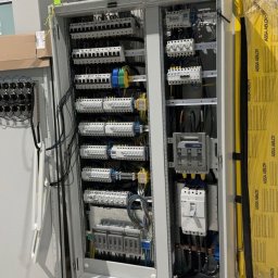 VoltSky Szymon Zaremba - Otwarta szafa sterownicza z rozdzielnicą elektryczną, widoczne bezpieczniki, kable i przewody, obok zapakowane płyty izolacyjne.