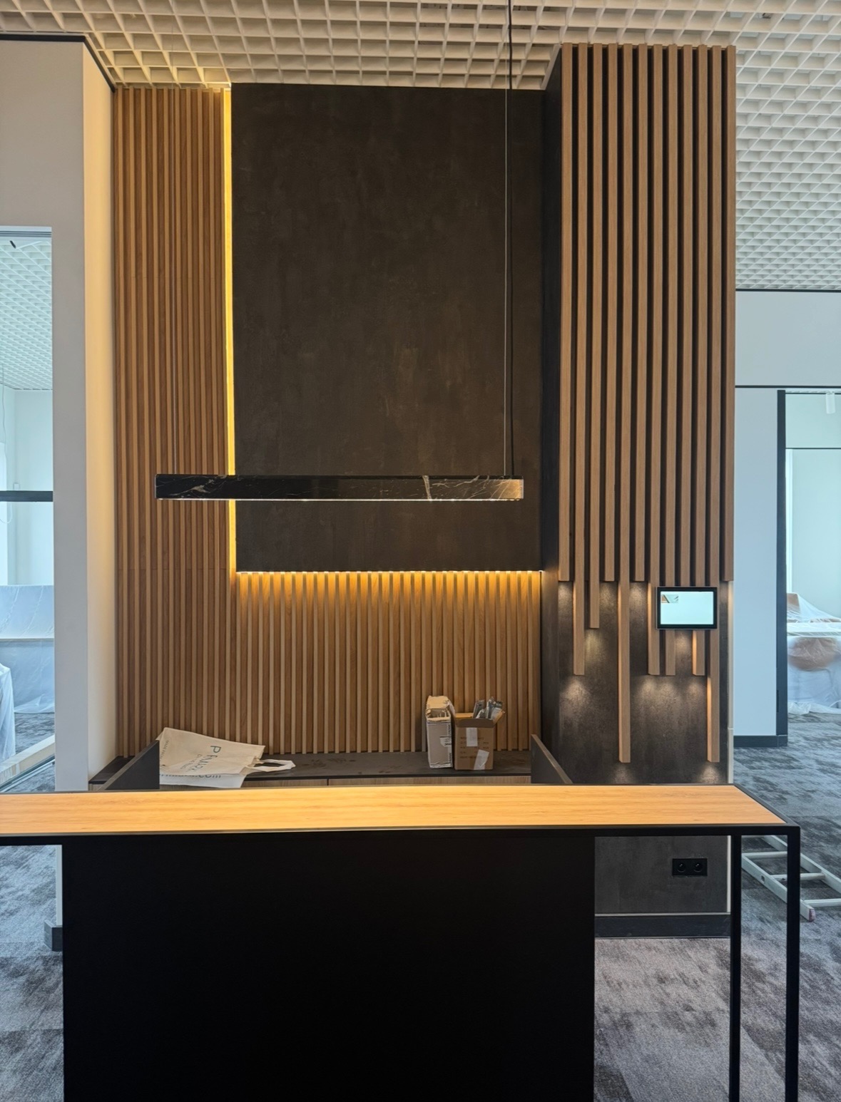 Nowoczesne oświetlenie biurowe: długa, marmurkowa lampa LED zawieszona nad blatem, podświetlone drewniane panele ścienne i sterownik oświetlenia.