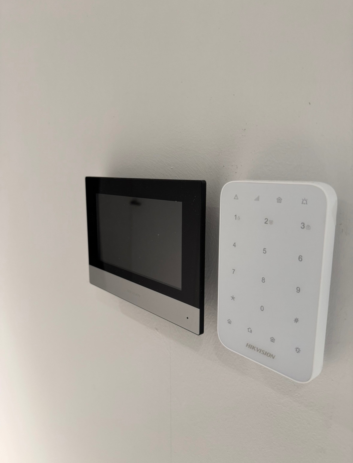 Panel dotykowy wideodomofonu Hikvision z klawiaturą numeryczną na białej ścianie, widok z boku.