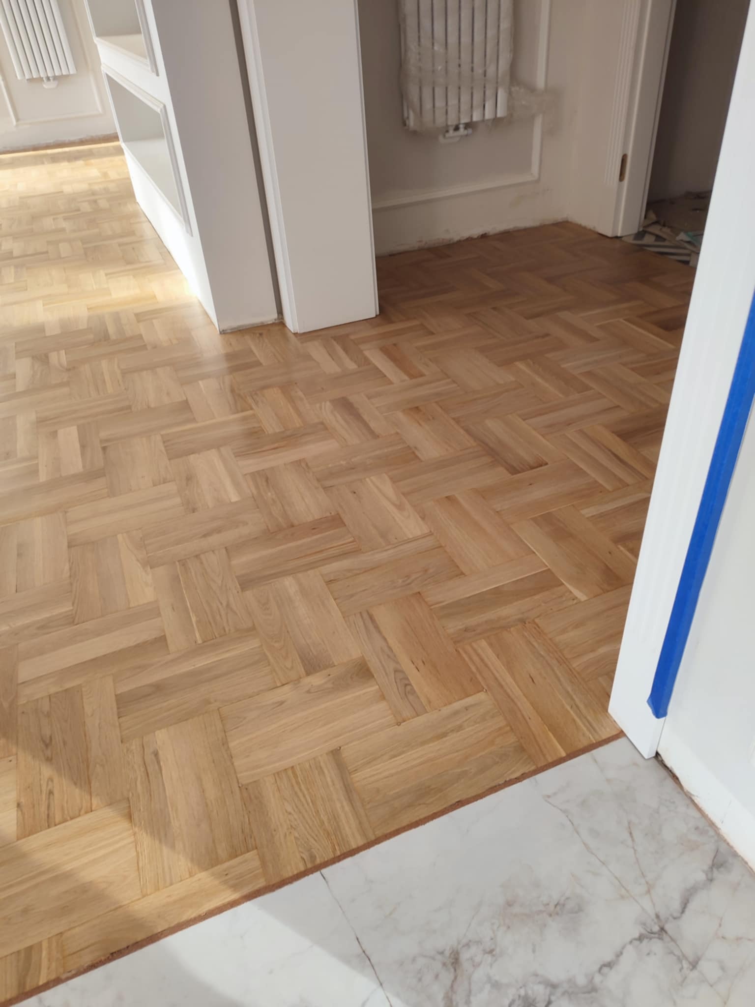 Ułożony parkiet w jodełkę francuską, widoczny fragment marmurowej podłogi w przejściu, zabezpieczone taśmą malarską ościeżnice.