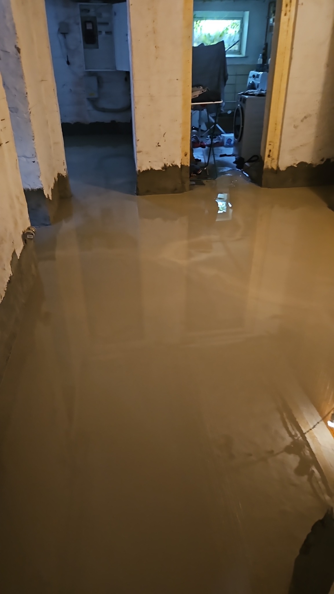 Wylewka samopoziomująca w piwnicy, widoczne ściany z fragmentami starego tynku i przejścia do innych pomieszczeń.