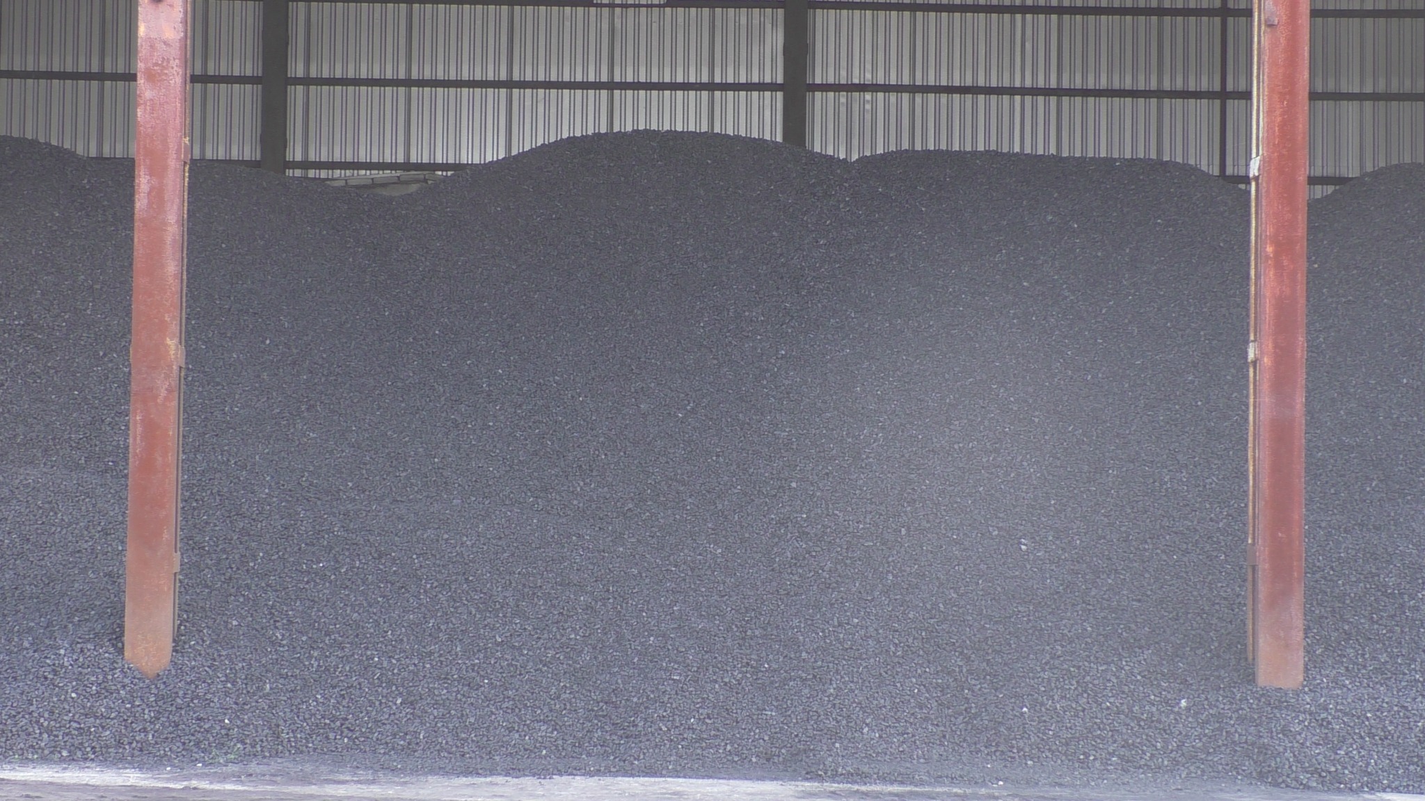 Duża pryzma antracytu pod zadaszeniem magazynu, widoczne metalowe podpory konstrukcji.