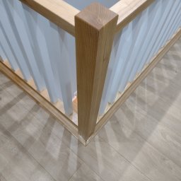 Wiktor Korejba VectorWood - Fragment narożnika balustrady z jasnego drewna i białych pionowych elementów, widoczny na tle podłogi z paneli.