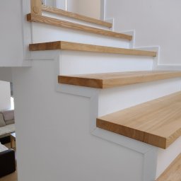 Wiktor Korejba VectorWood - Nowoczesne schody z jasnego drewna i białych elementów konstrukcyjnych, widoczne z bliskiej perspektywy, z fragmentem salonu w tle.