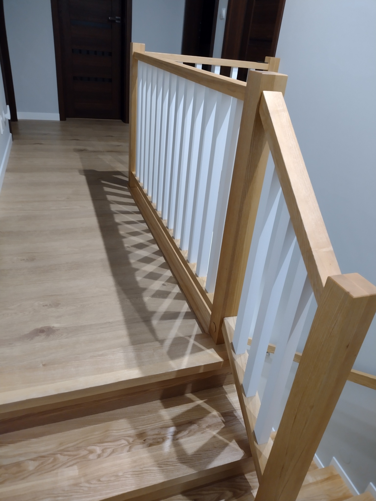 Jasne drewniane schody z balustradą z białymi tralkami, widok z góry na stopień, nowoczesny design.