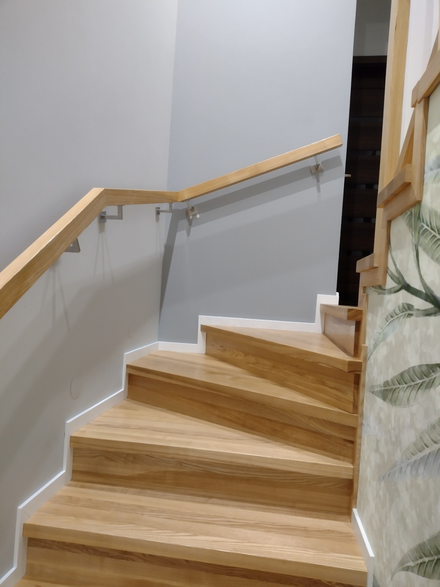 Kątowe schody z jasnego drewna z drewnianą poręczą zamocowaną do szarej ściany, widok z dołu.
