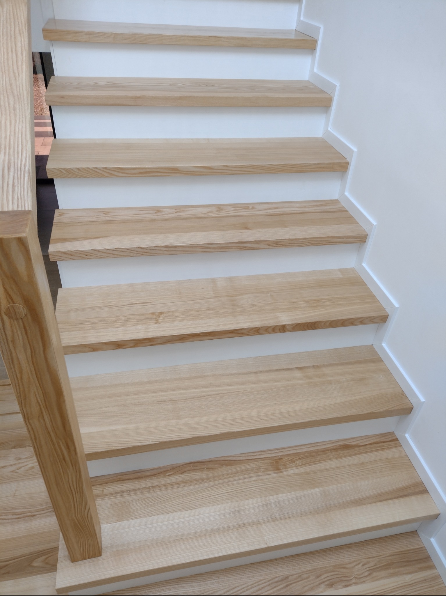 Jasne, drewniane stopnie schodów z białymi podstopnicami, widok z dołu, naturalne oświetlenie podkreśla strukturę drewna.