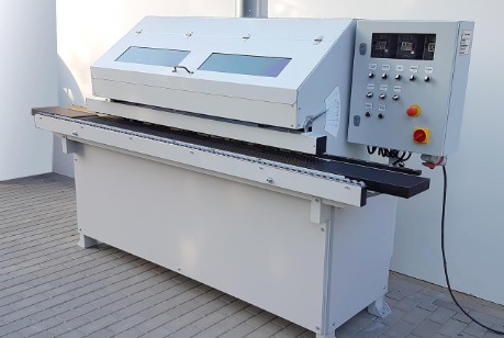 Profesjonalna, stacjonarna maszyna stolarska z panelem sterowania, widoczne elementy transportowe i osłony, ustawiona w jasnym pomieszczeniu.