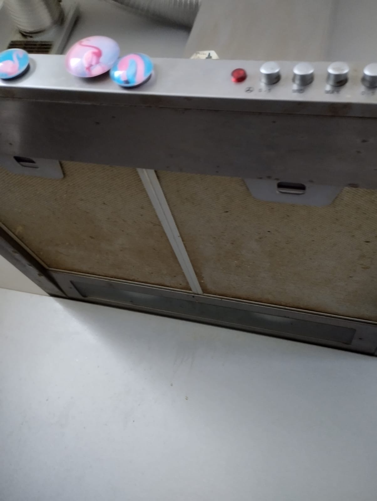 Brudny filtr okapu kuchennego z trzema magnesami na górze, widoczny z dołu.