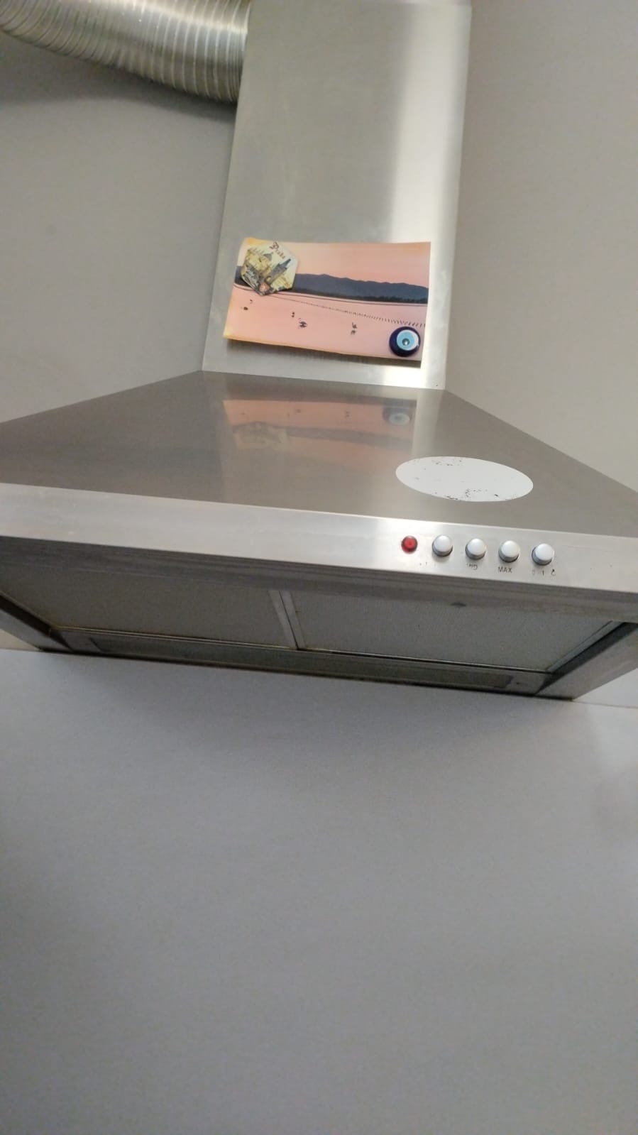 Metalowy okap kuchenny z naklejką przedstawiającą krajobraz i symbolem oka proroka, zamontowany na jasnej ścianie.