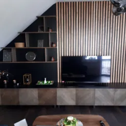 Nowoczesny salon z drewnianą ścianą z lameli, półkami pod skosem i szafką RTV z frontami w jodełkę.