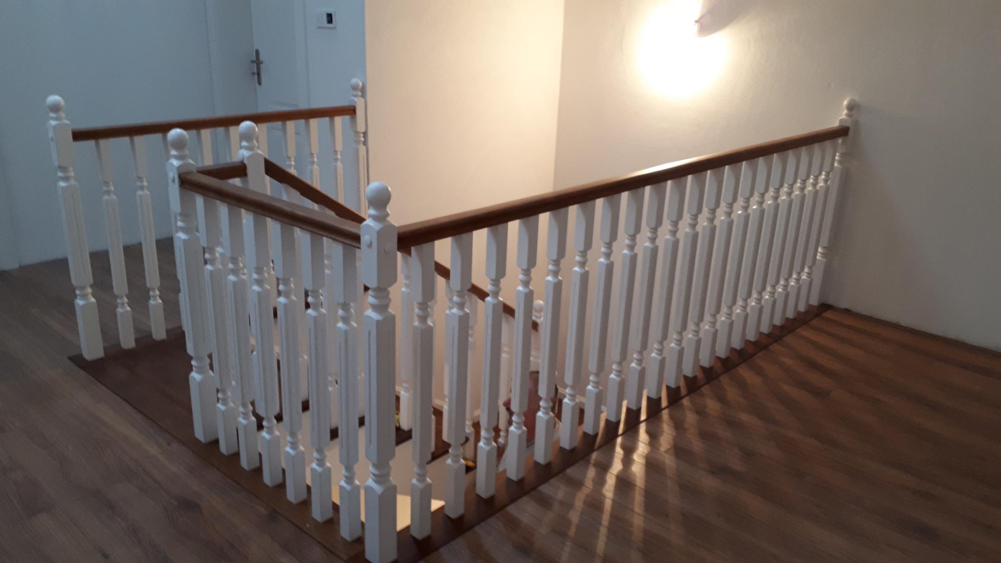 Klatka schodowa z drewnianymi balustradami w Kręgach Nowych. Białe tralki i brązowy poręcz, drewniana podłoga, widok z góry na dół.