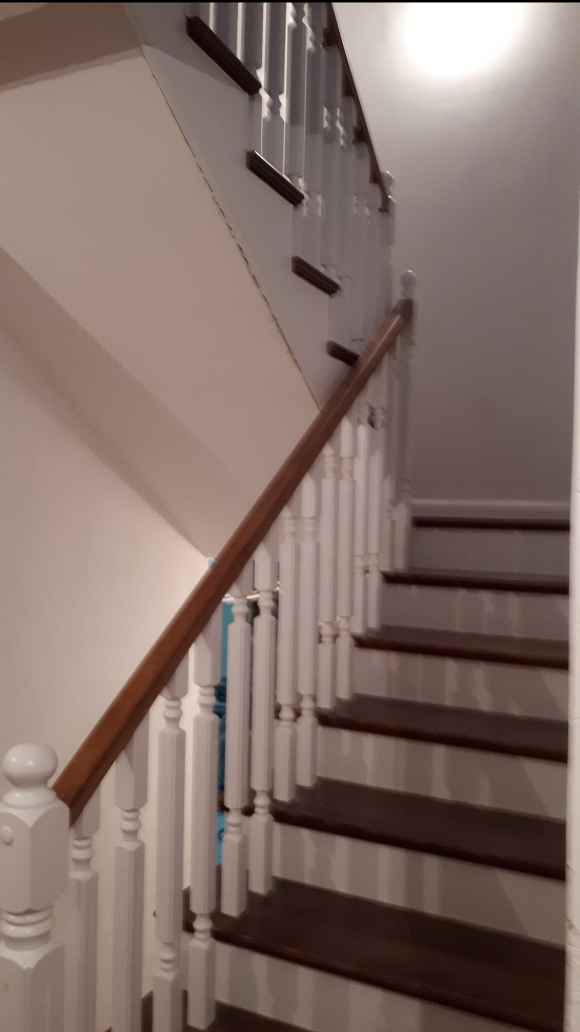 Klasyczne schody z drewnianymi stopniami i białą balustradą, widok z dołu w słabym oświetleniu.