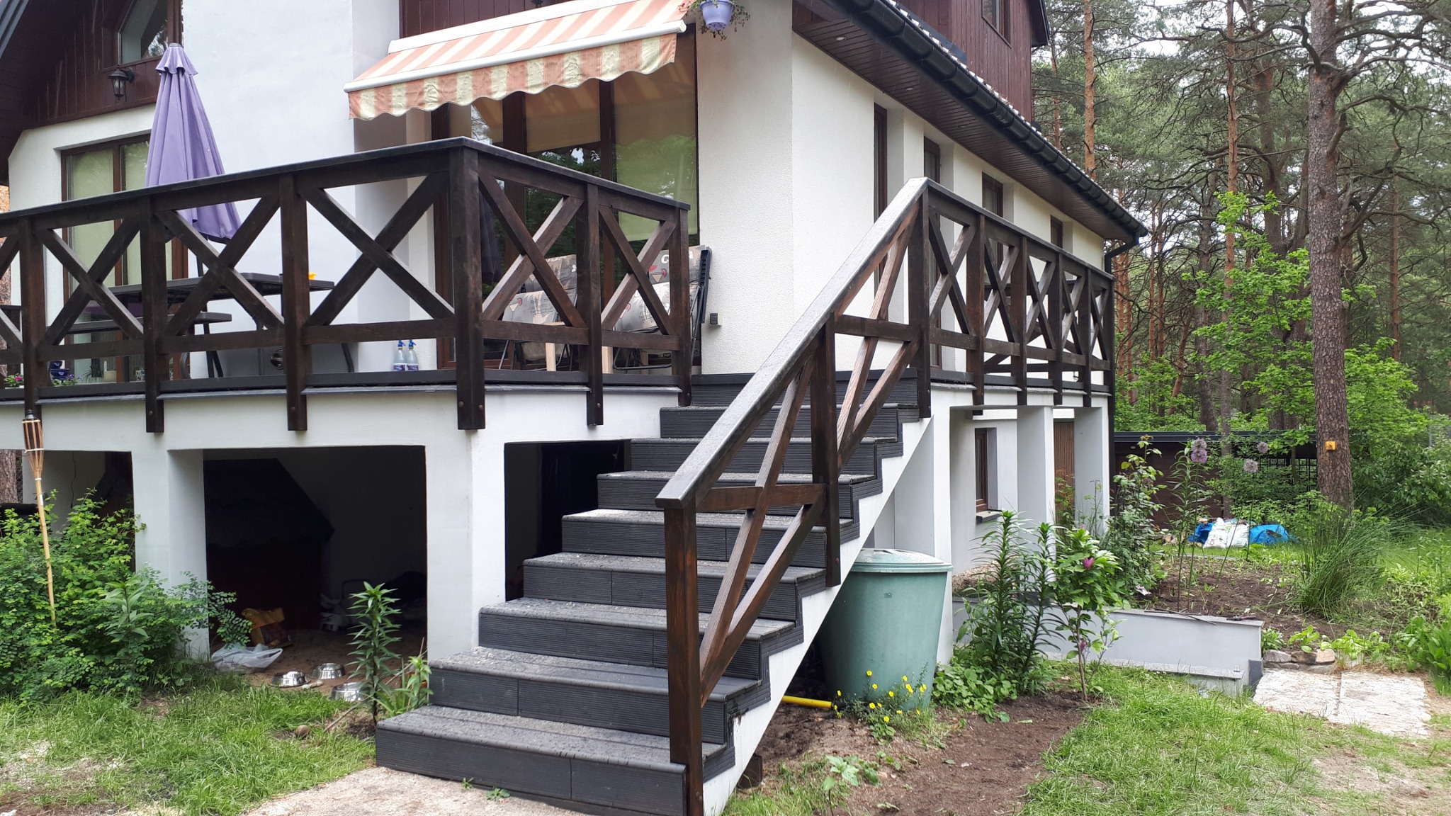 Zewnętrzne schody z ciemnoszarego kompozytu prowadzące na taras z ciemnobrązdką balustradą krzyżową, widok z dołu.