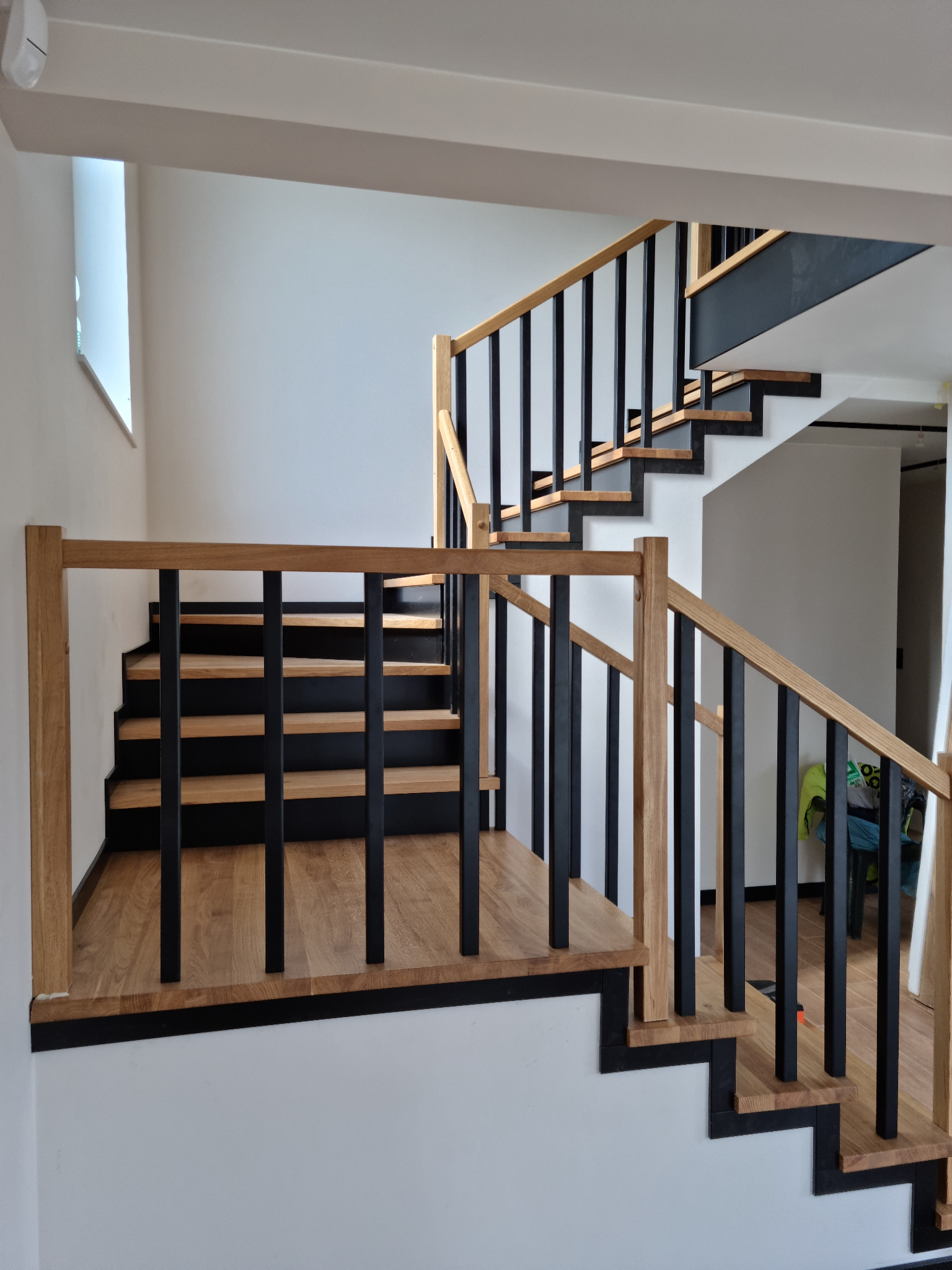 Nowoczesne schody drewniane z czarnymi balustradami i dębowymi stopniami, widok z dołu, jasne wnętrze, minimalistyczny design.