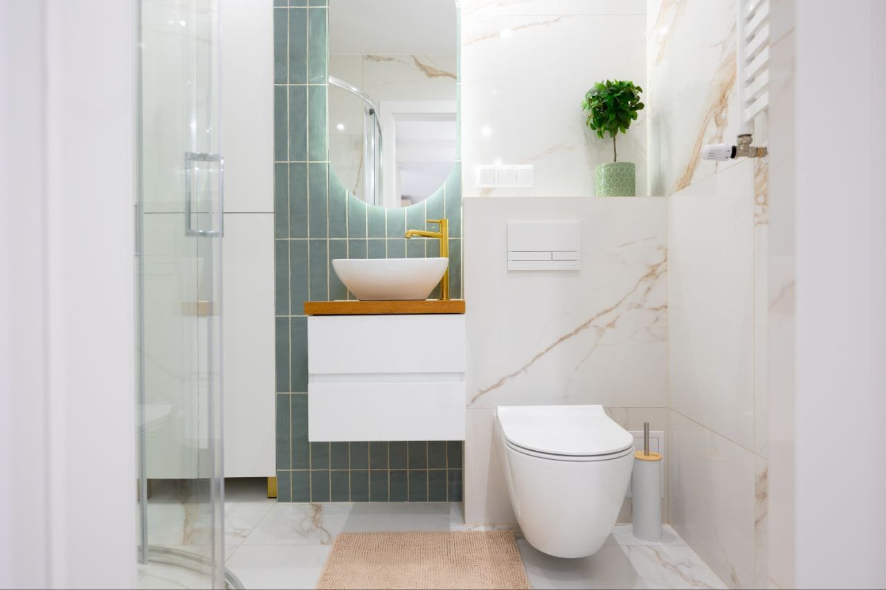 Nowoczesna łazienka z umywalką nablatową, złotą armaturą i zielonymi płytkami. Minimalistyczny design, białe marmurowe płytki i oświetlenie LED.