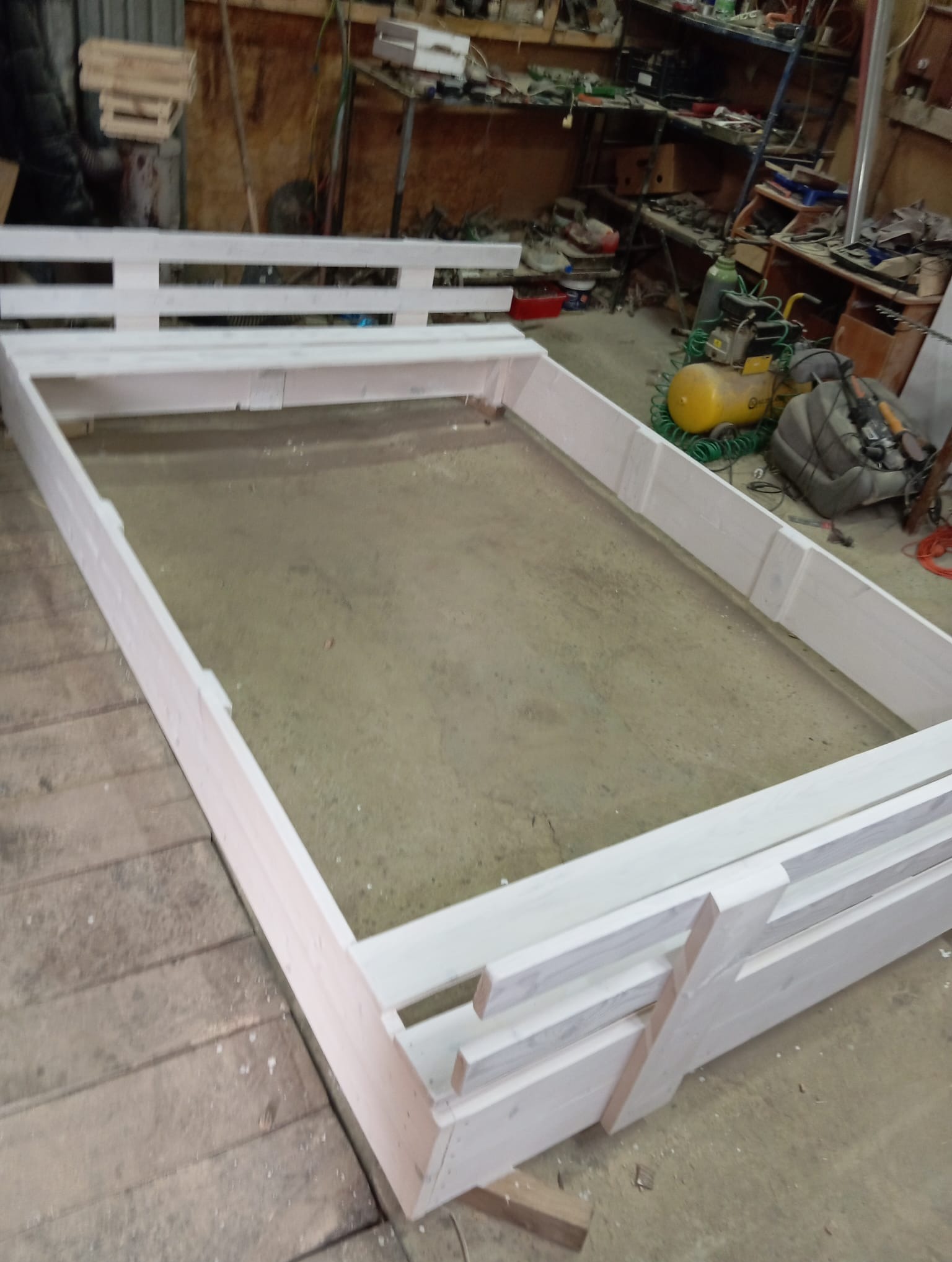 Drewniana konstrukcja w warsztacie, prawdopodobnie rama podwyższonego kwietnika lub element architektury ogrodowej, w trakcie budowy; widoczne narzędzia i materiały.