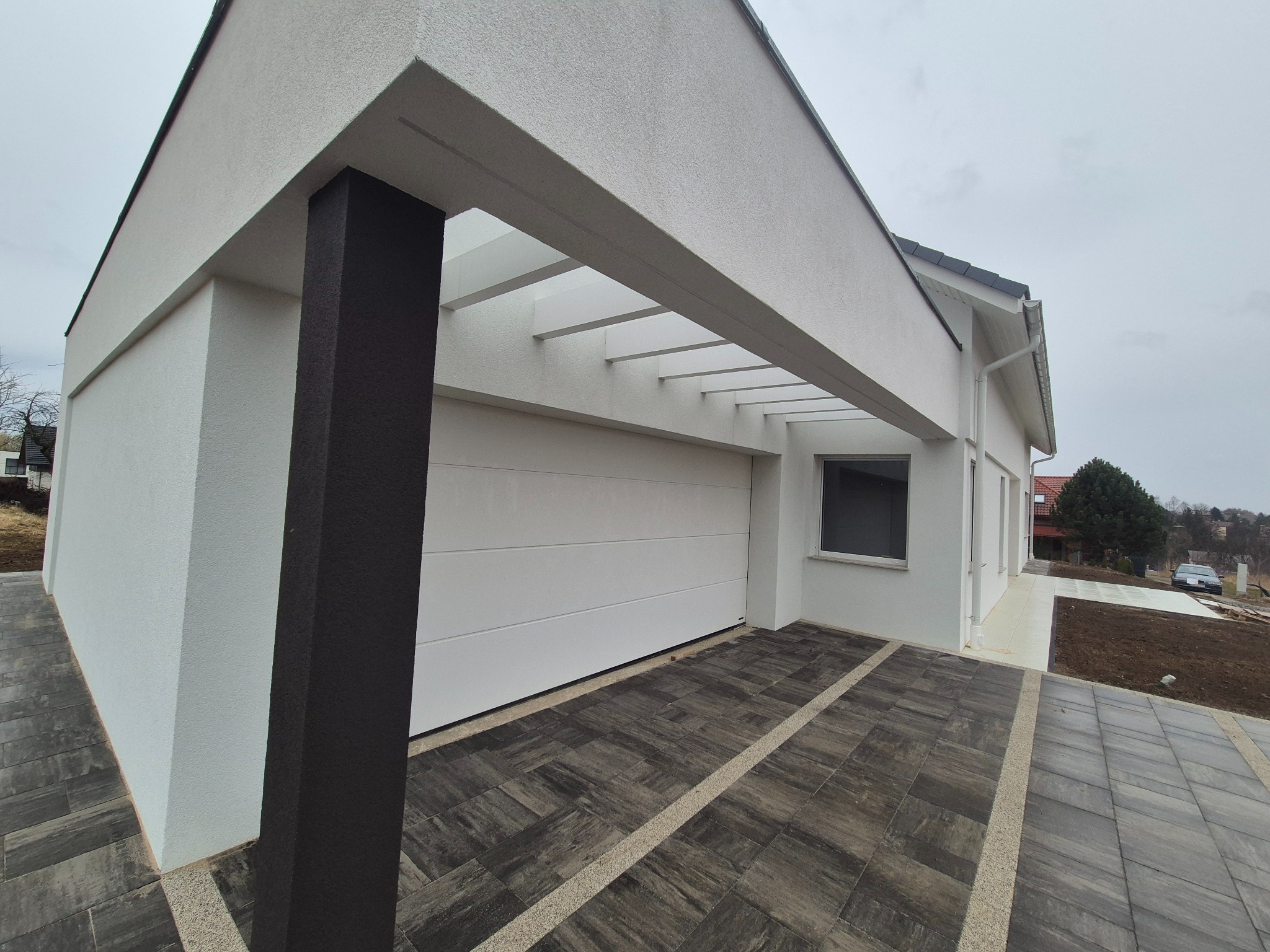 Nowoczesny dom jednorodzinny w Rzeszowie z białą elewacją i antracytowym akcentem kolumny, widok z zewnątrz na podjazd wyłożony kostką brukową.