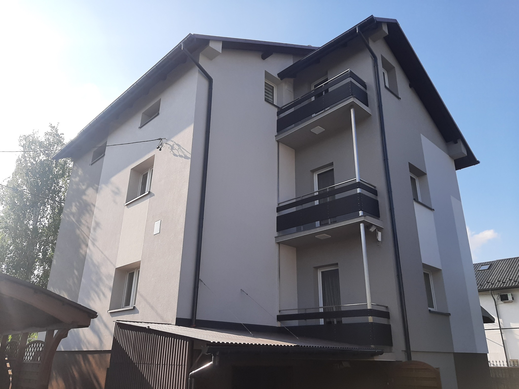 Nowoczesny, trzypiętrowy budynek z balkonami w szaro-białej kolorystyce, widoczny z perspektywy ulicy w słoneczny dzień.