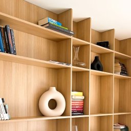 othe.studio - Drewniana, modułowa biblioteczka z książkami i dekoracyjnymi wazonami w różnych kształtach, oświetlona naturalnym światłem.