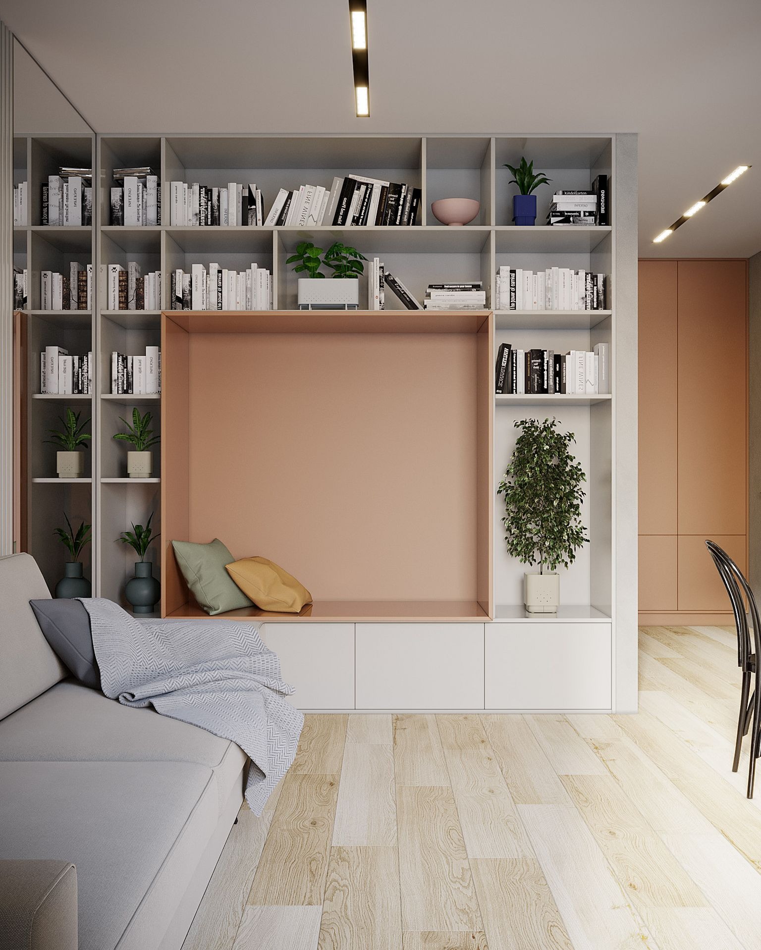 Nowoczesny salon z dużą, wbudowaną biblioteczką z otwartymi półkami, dekoracyjną wnęką w odcieniu brzoskwiniowym z poduszkami, i szarą sofą z narzutą w geometryczny wzór. Na półkach książki...