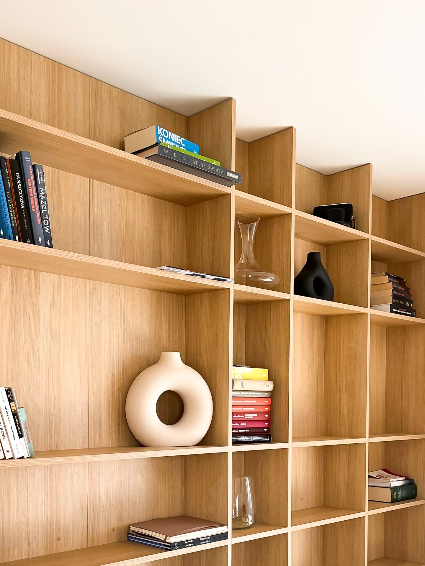 Drewniana, modułowa biblioteczka z książkami i dekoracyjnymi wazonami w różnych kształtach, oświetlona naturalnym światłem.