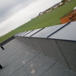 Zaklad Blacharsko-Dekarski - Widok z góry na płaski dach pokryty papą z kominkami wentylacyjnymi, w tle zielone pole i zabudowania.