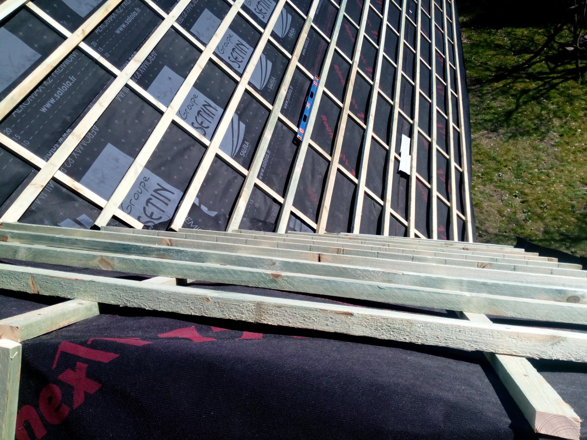 Konstrukcja drewniana pod nowy dach z membraną w Nakle nad Notecią, widoczny poziomica i fragment zieleni w tle.