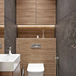 Evga - Nowoczesna łazienka z drewnianymi panelami ściennymi i szarą, kamienną okładziną, wisząca toaleta, umywalka nablatowa i szafka wisząca z podświetleniem LED tworzą spójną aranżację.