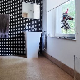 METAINVEST SPÓŁKA Z OGRANICZONĄ ODPOWIEDZIALNOŚCIĄ - Nowoczesna łazienka z umywalką wolnostojącą na tle ściany w czarno-białą kratę. Lustro w metalowej ramie, roleta w oknie, podłoga z kamienia.