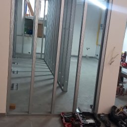 METAINVEST SPÓŁKA Z OGRANICZONĄ ODPOWIEDZIALNOŚCIĄ - Konstrukcja z metalowych profili, tworząca szkielet ścian działowych w pomieszczeniu. Widoczne narzędzia i płyta. Etap prac przygotowawczych.