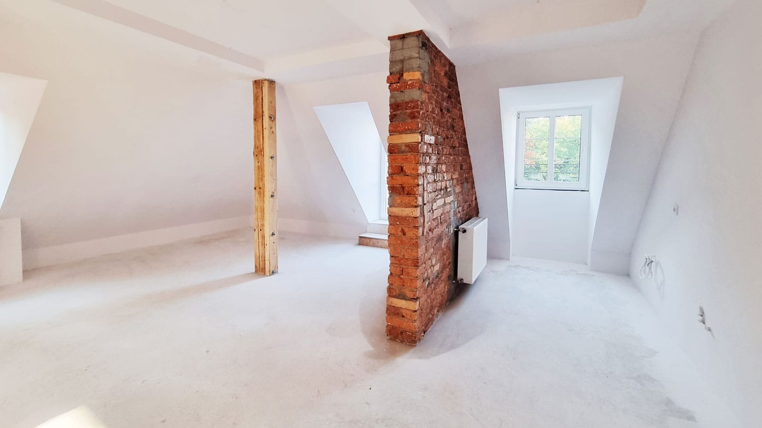 Poddasze po remoncie: białe ściany, ceglana ścianka działowa z grzejnikiem, drewniany słup. Widoczne okna dachowe i świeżo wylana posadzka.