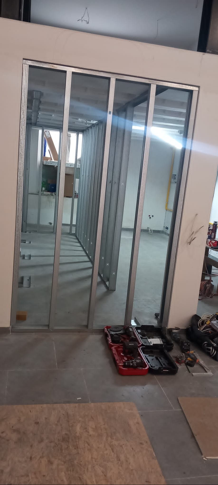 Konstrukcja z metalowych profili, tworząca szkielet ścian działowych w pomieszczeniu. Widoczne narzędzia i płyta. Etap prac przygotowawczych.