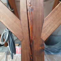 Fragment drewnianej konstrukcji dachu z widocznymi elementami więźby, zabezpieczonymi folią i przewodami elektrycznymi.